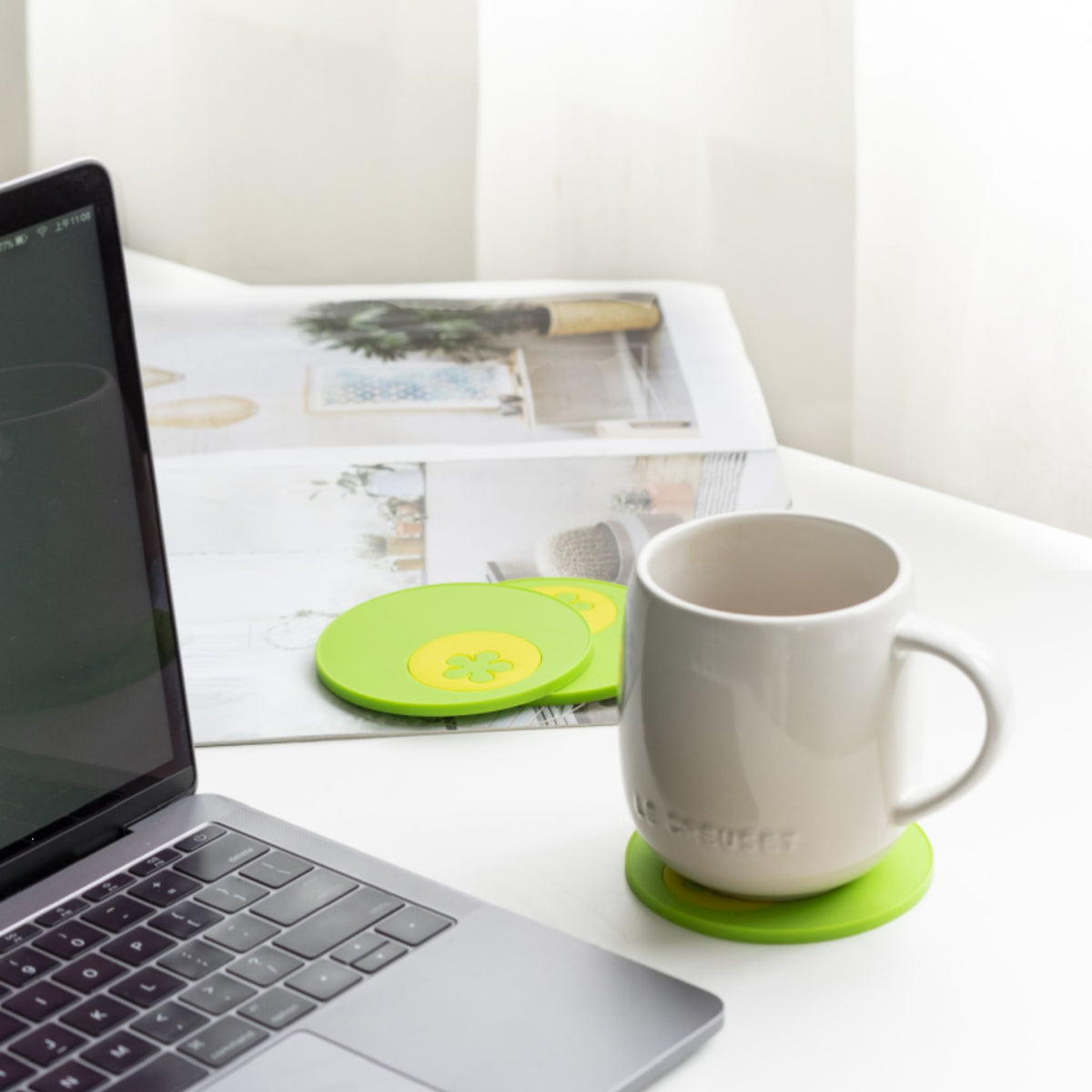 Runder, limettengrüner Multiuntersetzer mit Tasse auf hellem Tisch neben Laptop.