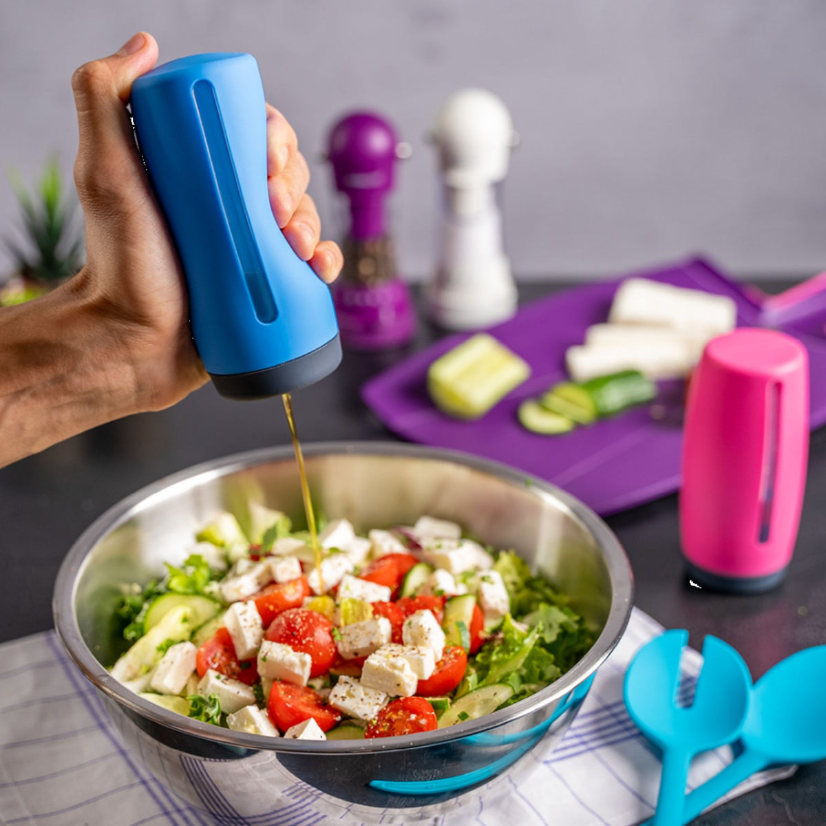 Anthrazitfarbener Dosierspender gibt Öl über frischen Salat mit Feta und Tomaten ab.