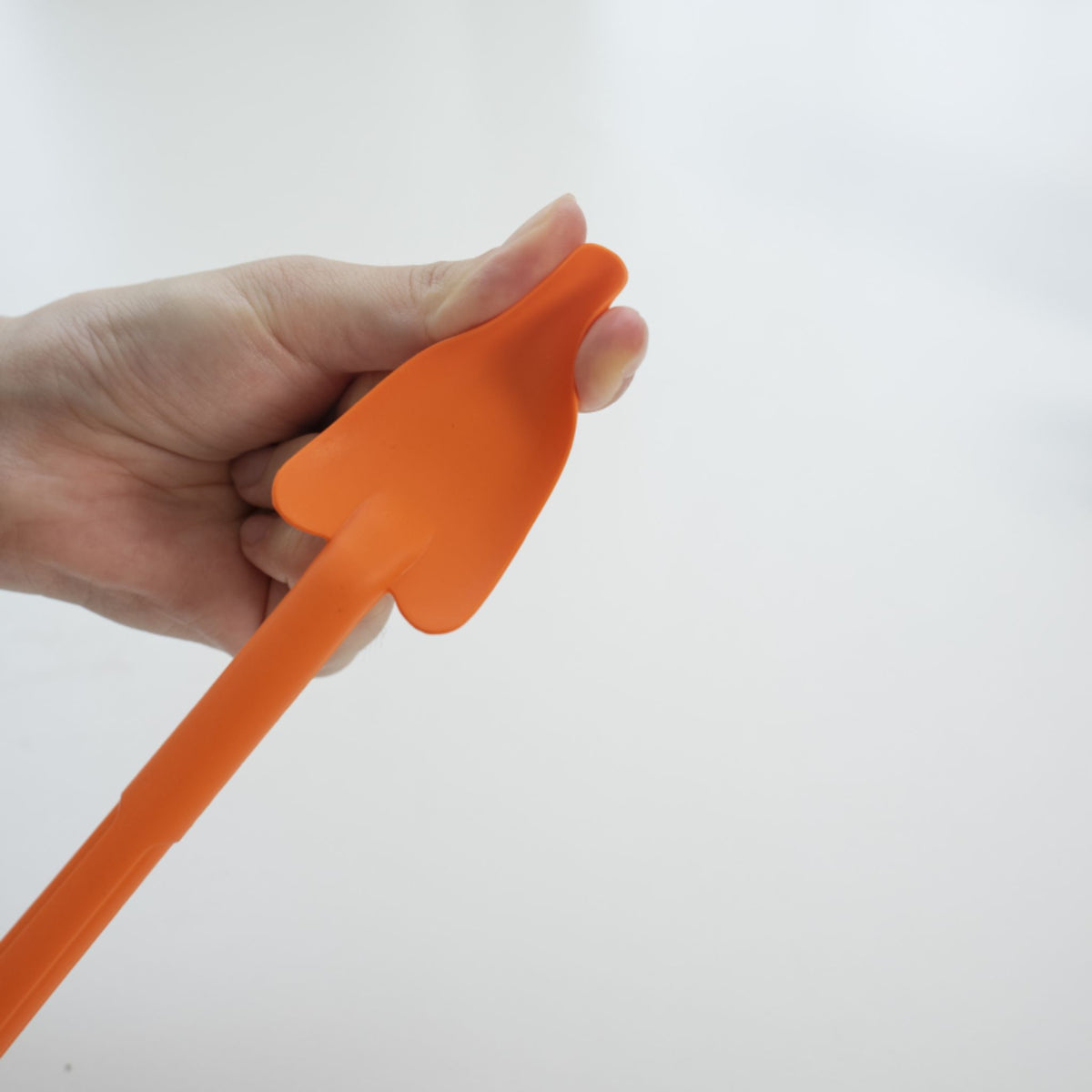 Hand hält orangen Restelöffel mit breiter, flacher Laffe aus Silikon.