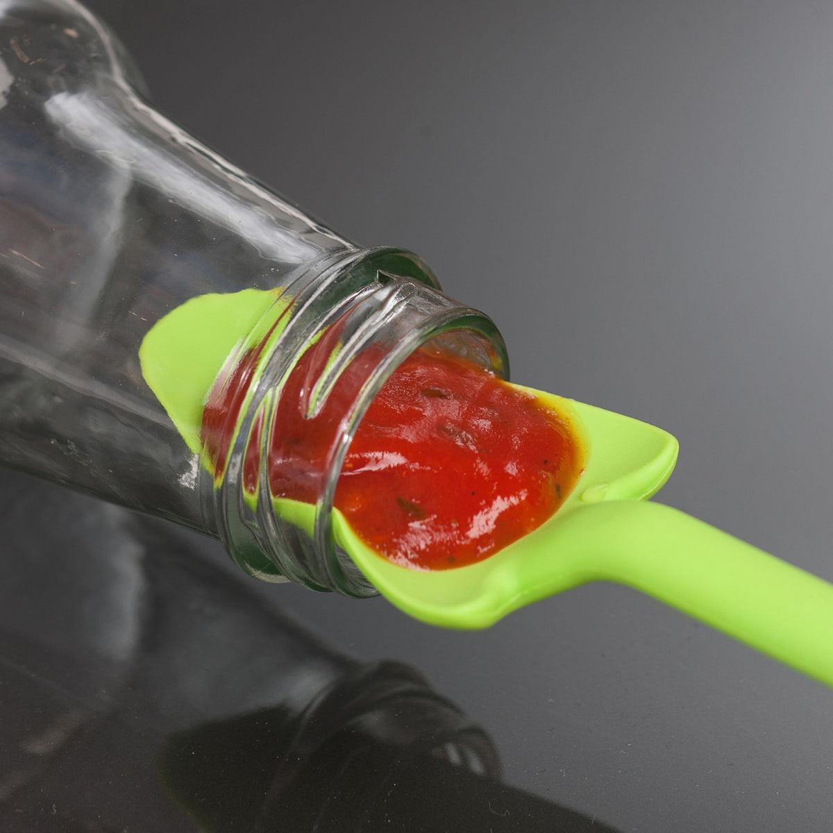 Limettengrüner Restelöffel aus Silikon mit eingegossener Tomatensauce aus Glasflasche.