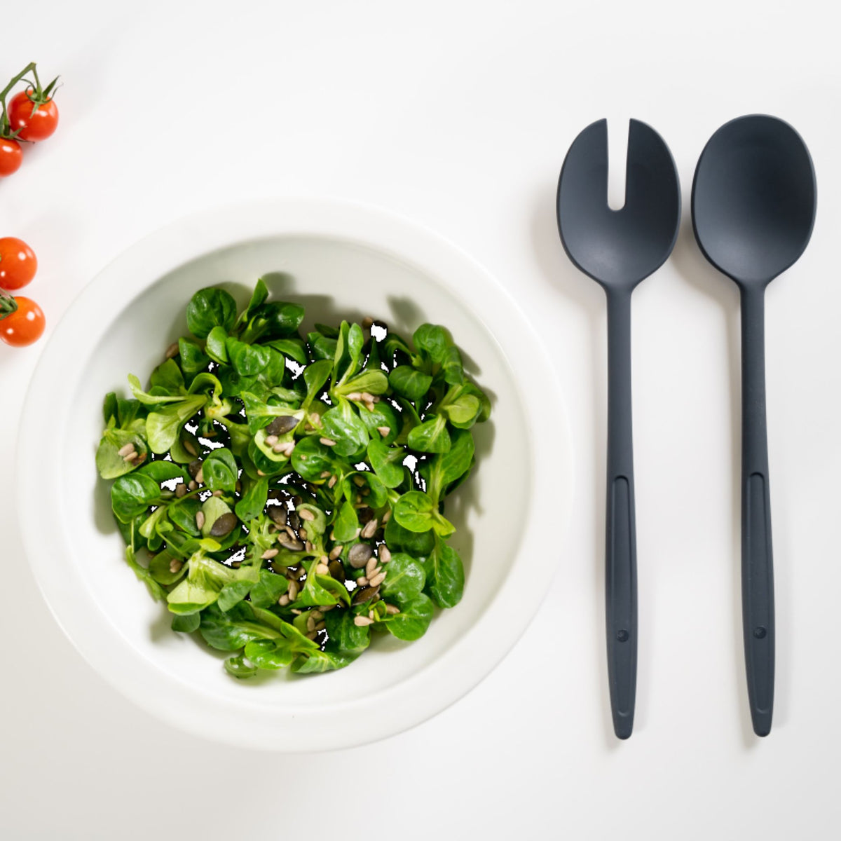 Anthrazitfarbenes Salatbesteck aus Kunststoff neben weißer Schale mit grünem Salat.
