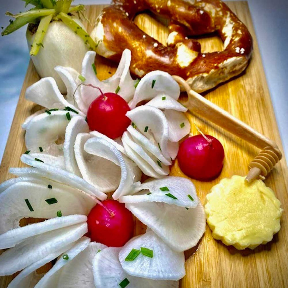 Weißer Spiralschneider mit dünnen Gemüsestreifen, Radieschen und Butterornament auf Holzbrett.