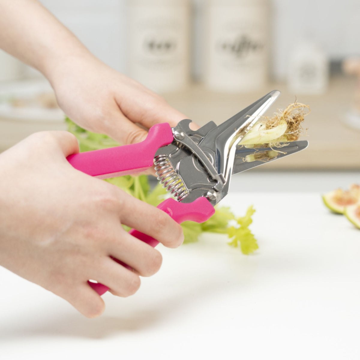 Küchenschere mit pinkfarbenen Griffen schneidet getrocknete Kräuter auf weißer Arbeitsfläche.