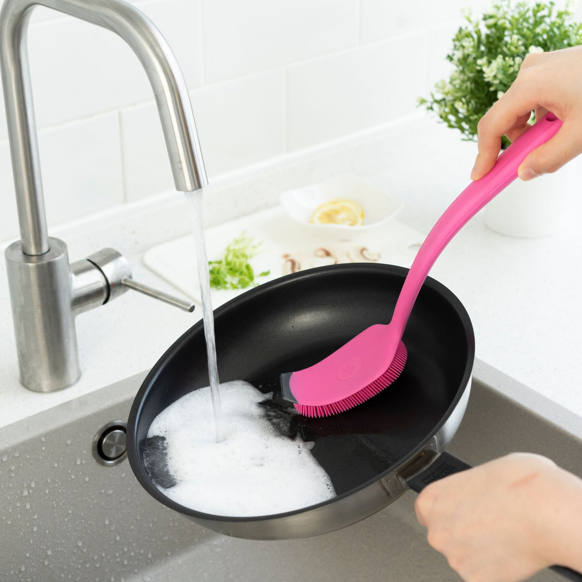 Spülbürste in Pink mit ergonomischem Griff, wird zum Reinigen einer schwarzen Pfanne verwendet.