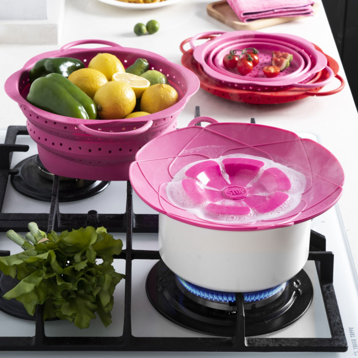 Kochblume XL Dampfgarer aus Silikon in Pink auf Herd mit weißem Topf und frischem Gemüse innen.