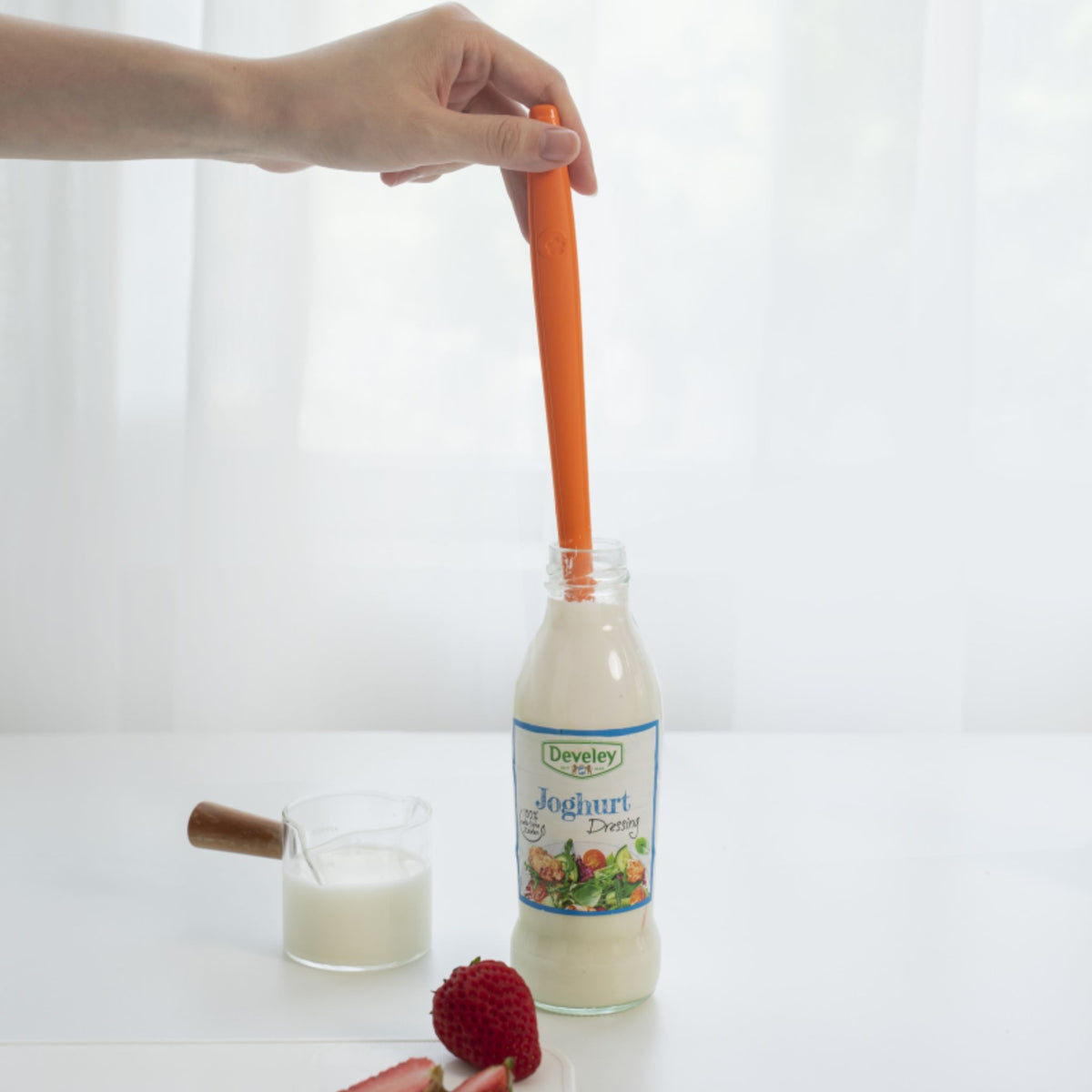 Anthrazitfarbener Restelöffel taucht in eine Joghurtflasche, daneben Glas mit Joghurt.