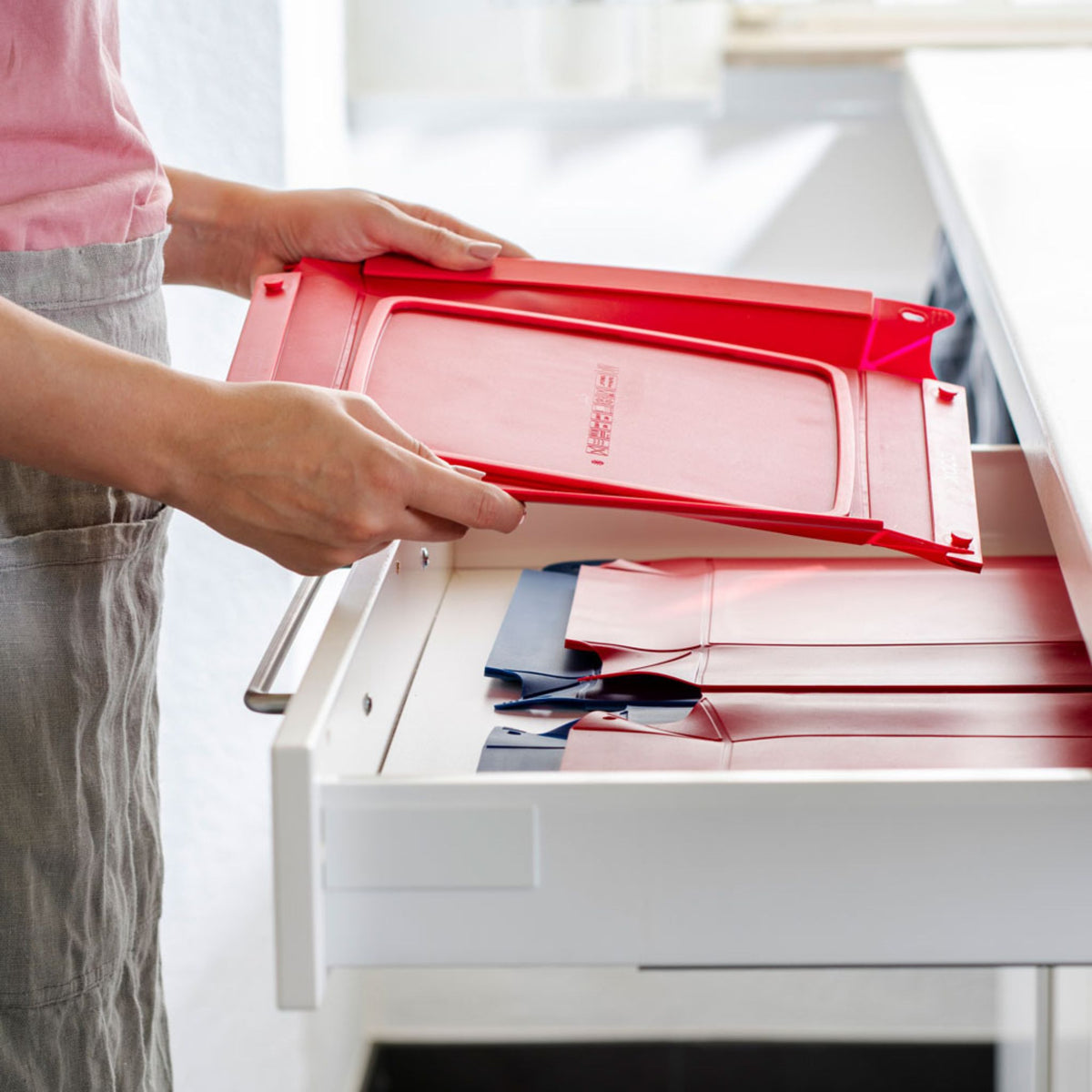 Rote flexible Küchenmatte aus Silikon mit Griffen, die in Schublade gelegt wird.