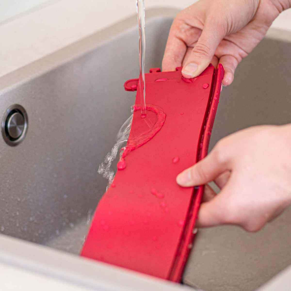 Rote, abnehmbare Dichtung der Coox Springform wird unter fließendem Wasser gereinigt.