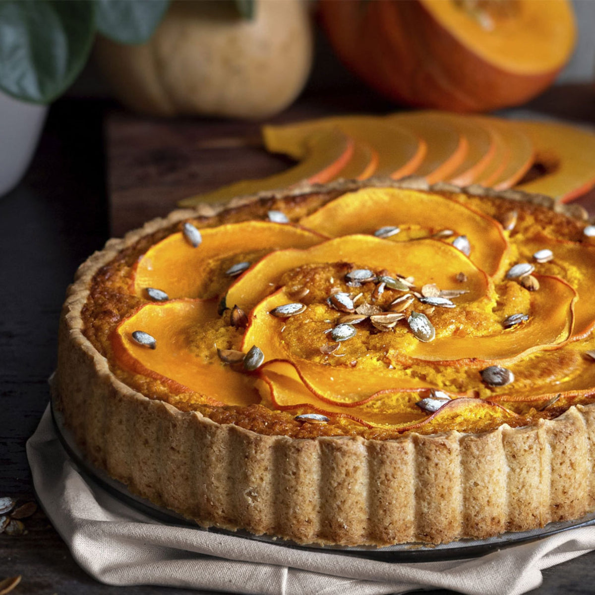 Quiche mit Kürbisscheiben und Kürbiskernen in goldbrauner Quicheform aus Keramik.