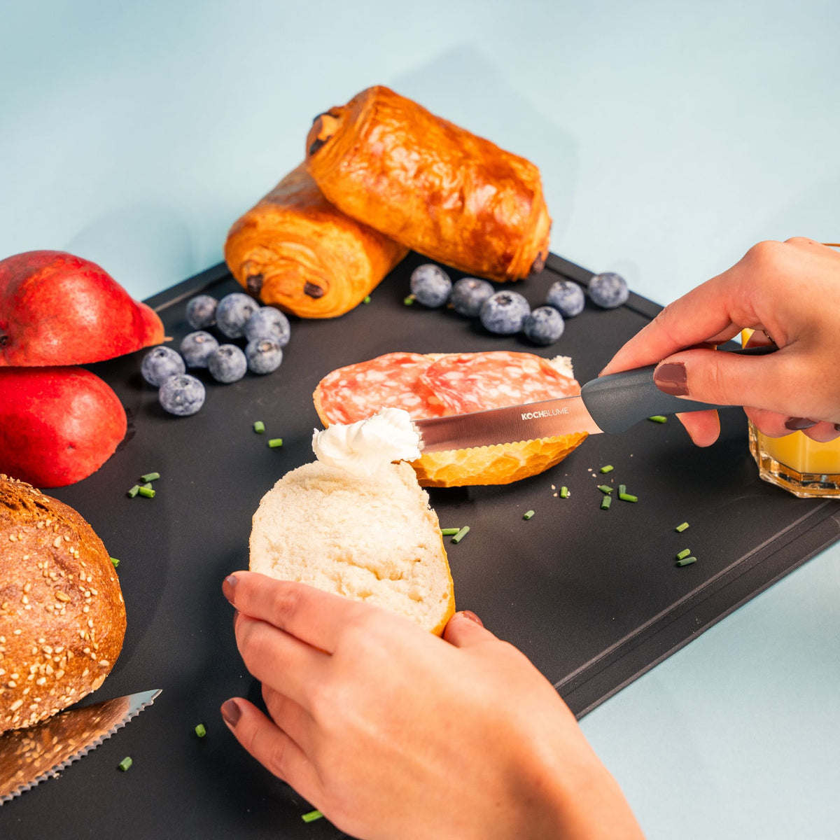 Frühstücksmesser mit schwarzem Griff schneidet Brötchen auf schwarzem Schneidebrett.