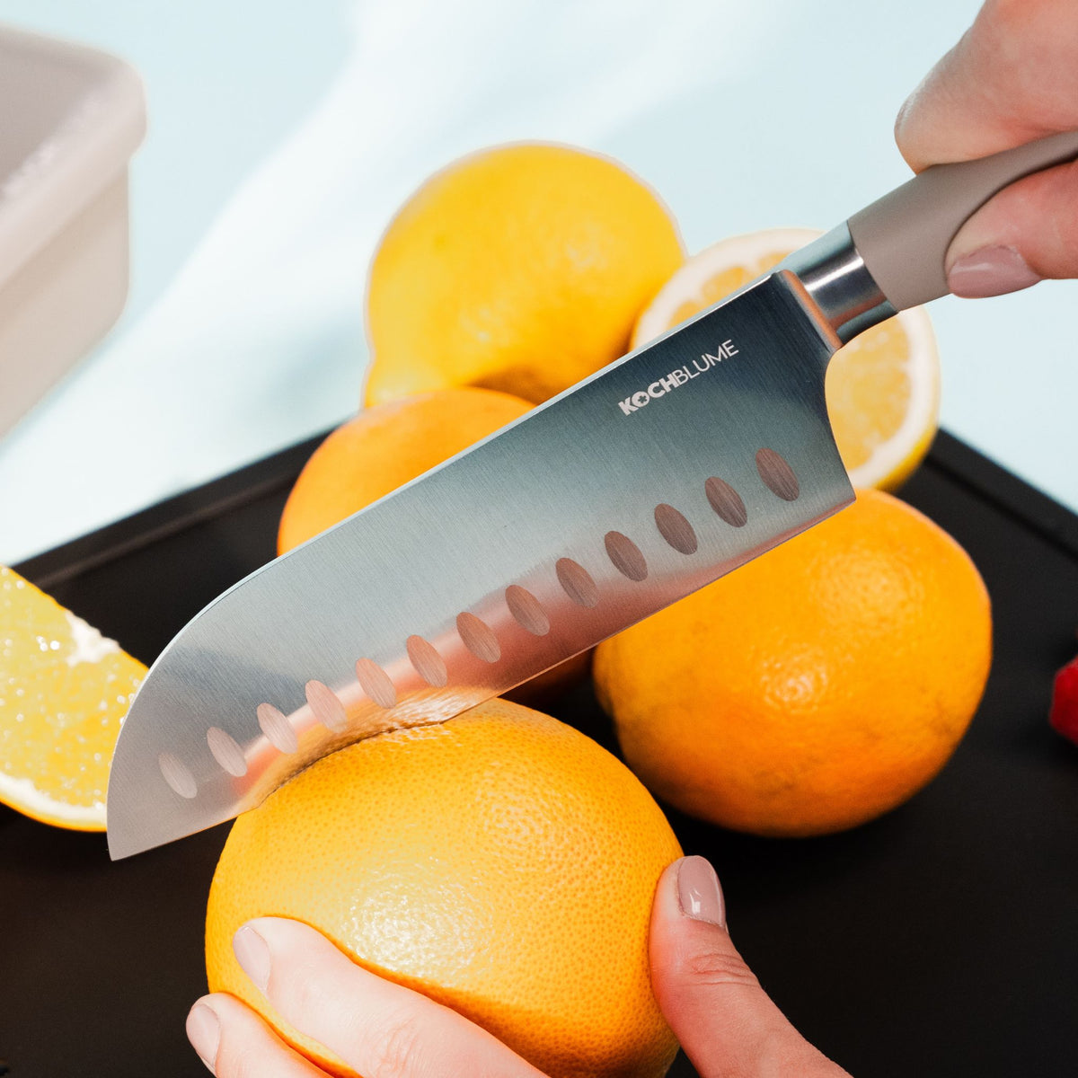 Santokumesser mit anthrazitfarbener Klinge schneidet Grapefruit auf schwarzem Untergrund.