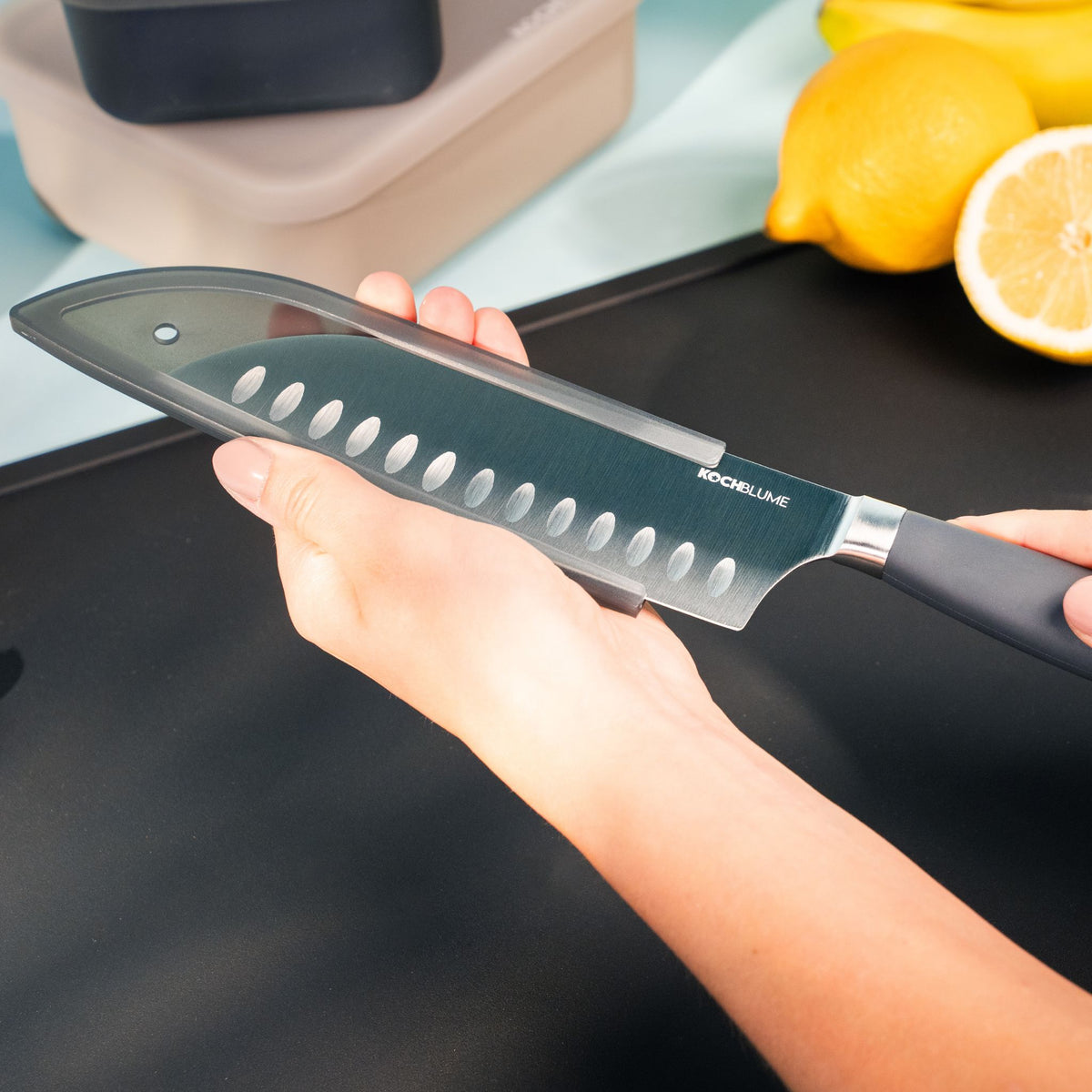 Santokumesser mit anthrazitfarbenem Wellenschliff und ergonomischem Griff in Hand gehalten.