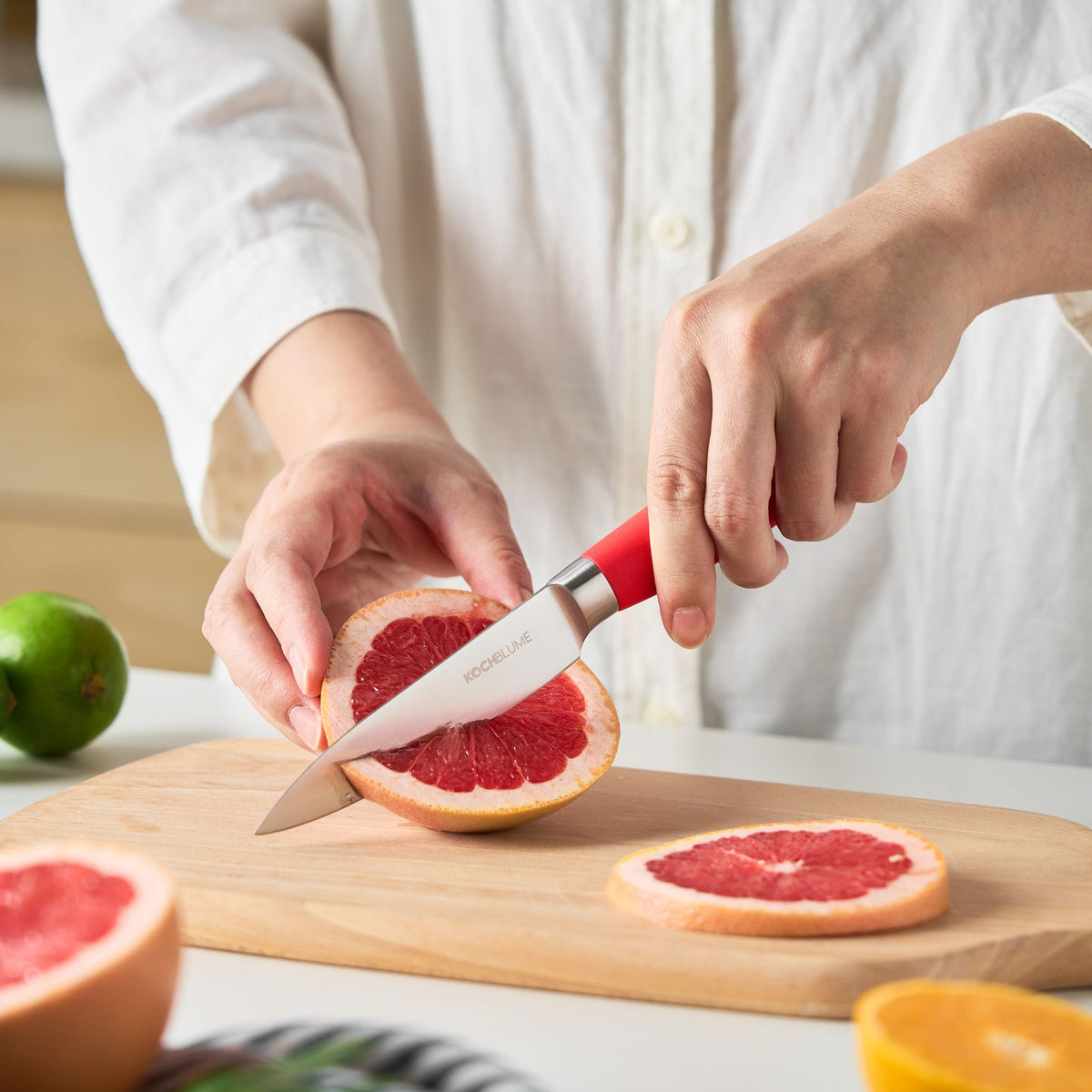 Gemüsemesser mit anthrazitfarbenem Griff schneidet Grapefruit auf Holzbrett.