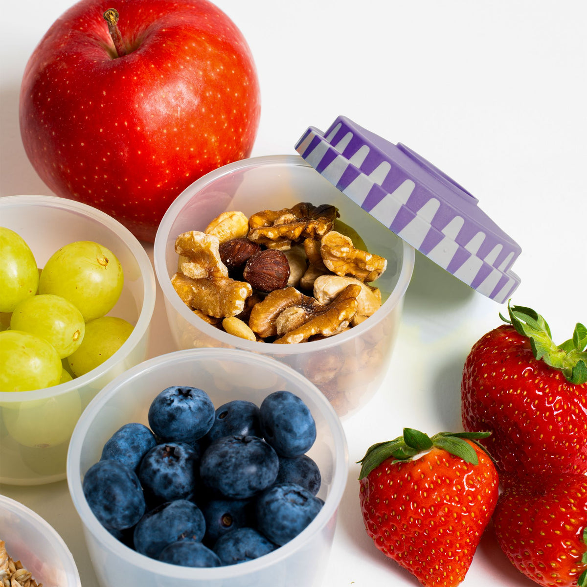 Sechsteiliges Deckelset in verschiedenen Farben mit Lebensmitteln gefüllten Dosen und frischem Obst.